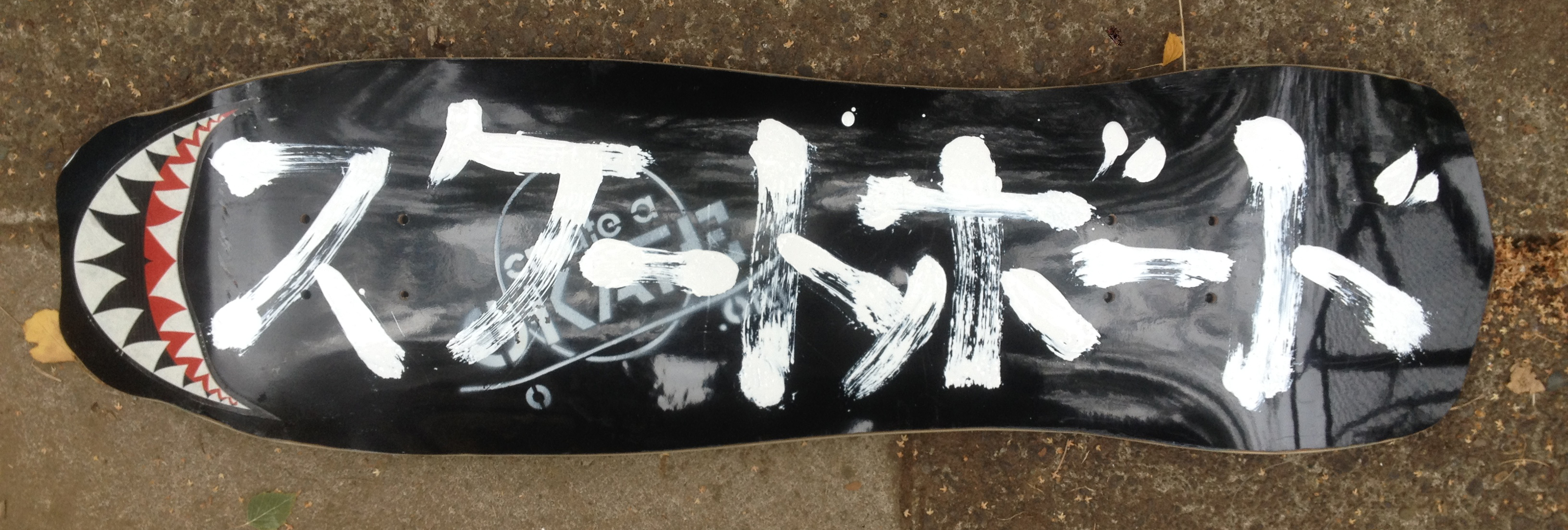 Suke-to Bo-do the japanese pronunciation of skateboard brush lettered Katakana letters in white enamel on a black hammerhead and diamond tailed skateboard I cut out at a demo for Create a Skate a few years ago