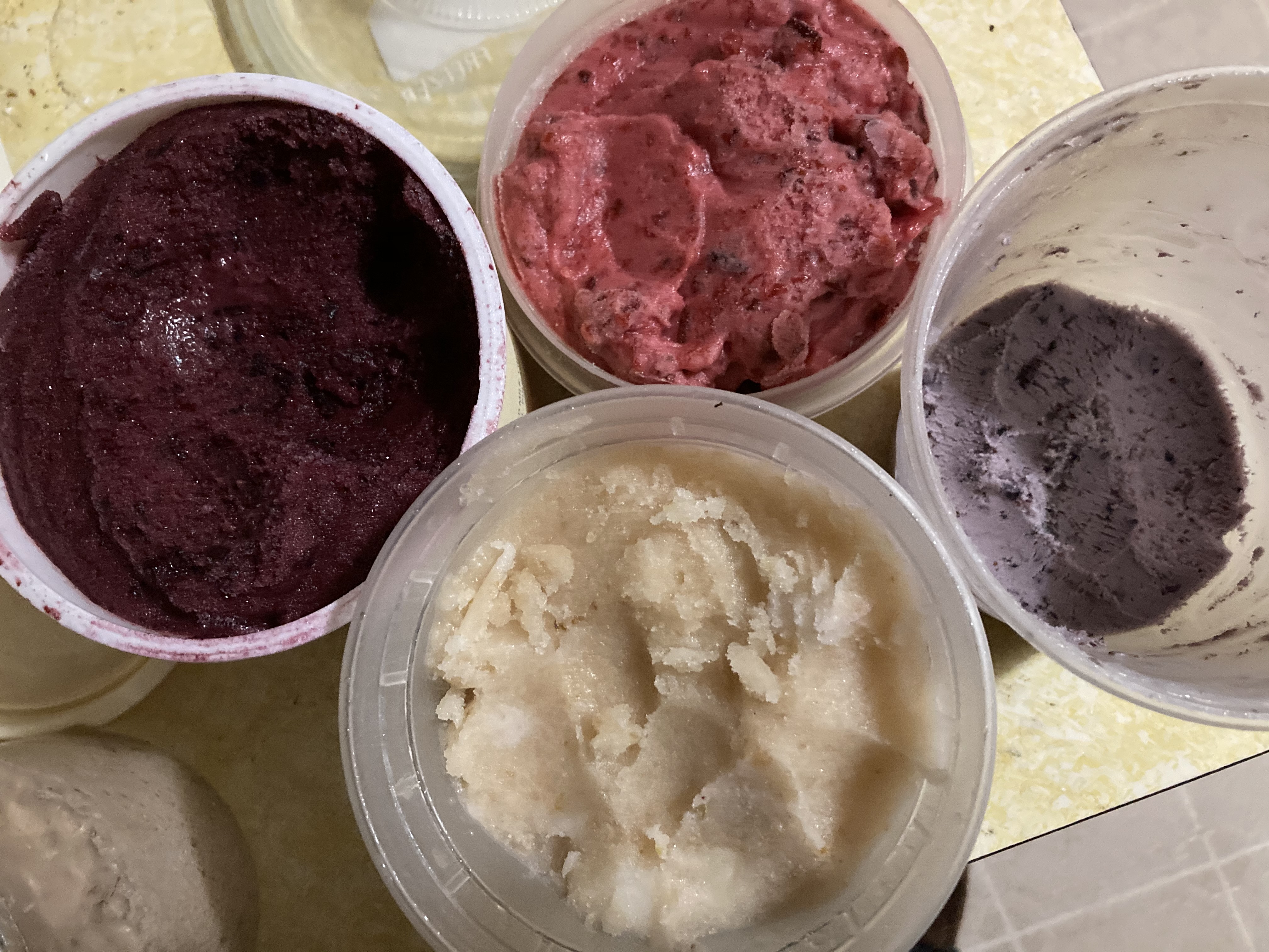 Three plastic containers with different colored homemade sherbet and one of homemade ice-cream. Dark purple grape, lighter red violet Italian Prune, Pale yellow pear and light lavender blueberry ice-cream that's almost gone